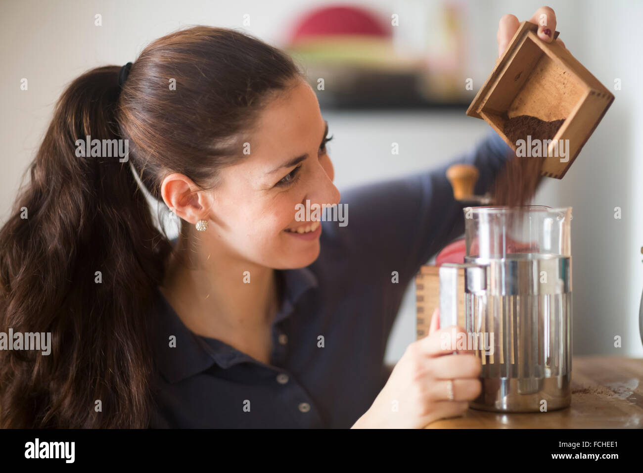 Donna sorridente versando la polvere di caffè in vetro caffè Foto Stock
