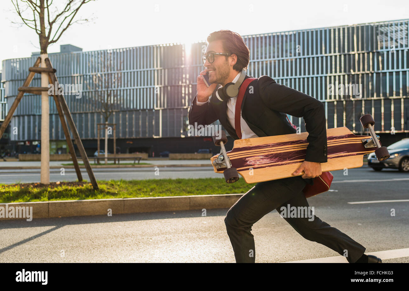 Germania Frankfurt giovane imprenditore skateboard in esecuzione sotto il suo braccio utilizzando il telefono cellulare Foto Stock