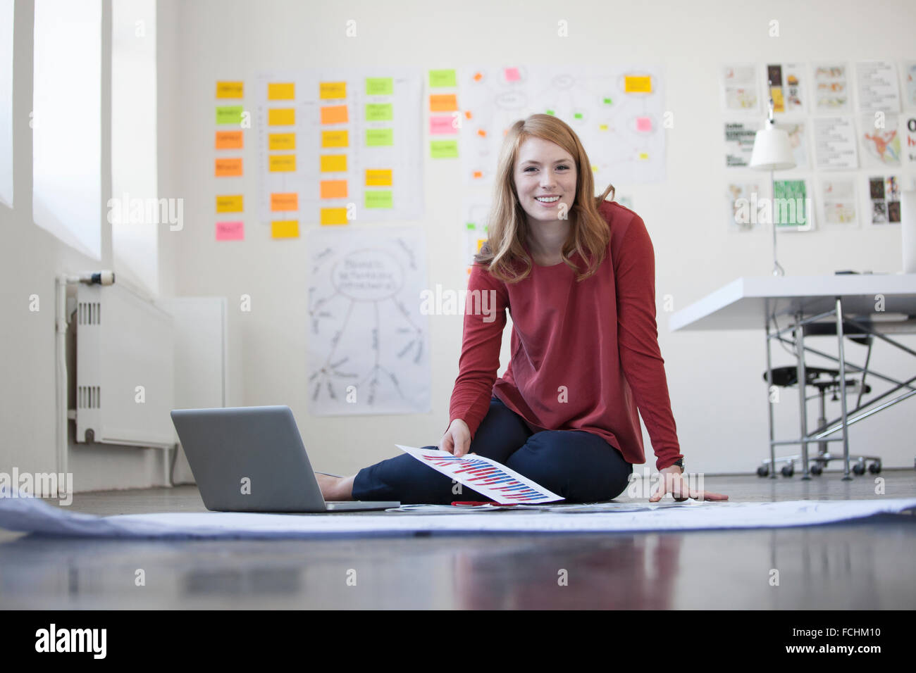 Giovane donna in ufficio seduti sul pavimento lavora attraverso carte Foto Stock