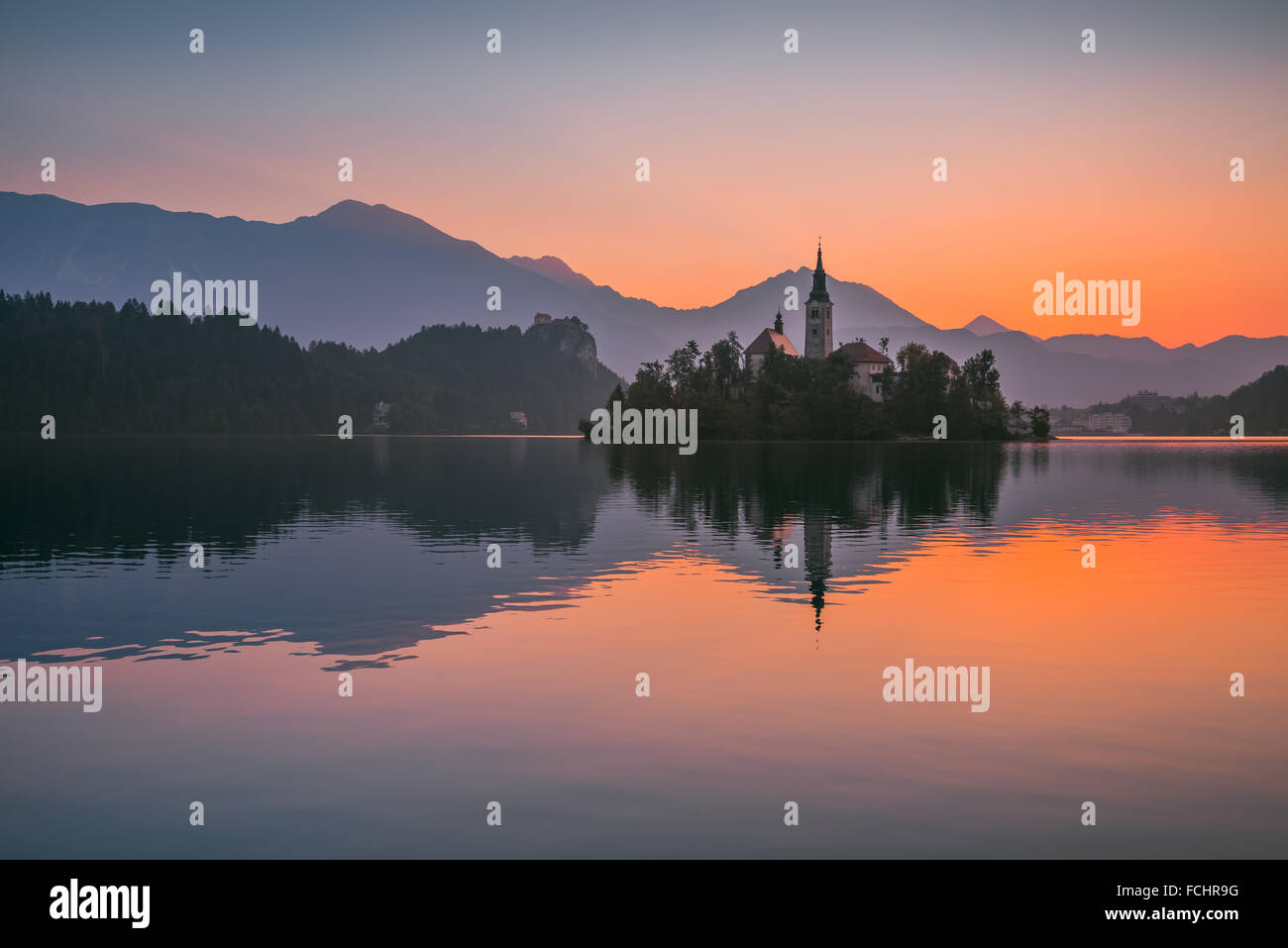 La piccola isola con la Chiesa cattolica nel lago di Bled, Slovenia all'alba con il castello e le montagne sullo sfondo Foto Stock