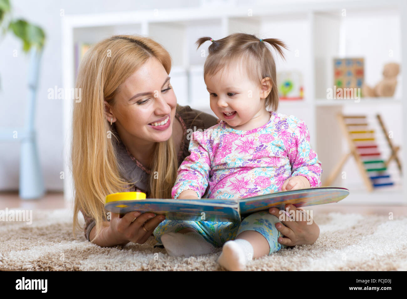 Madre felice di leggere un libro per bambini ragazza in ambienti interni Foto Stock