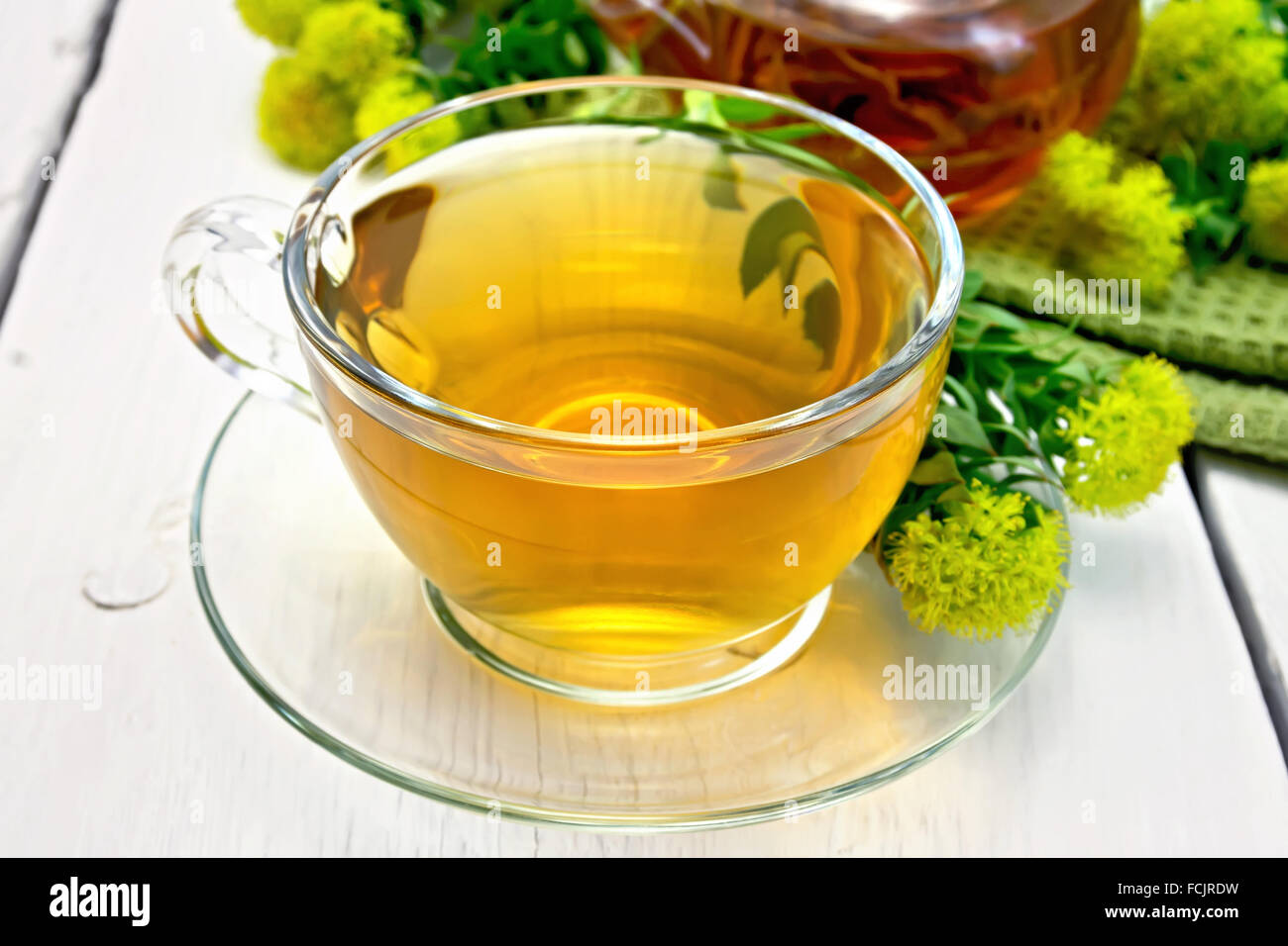 Il tè alle erbe in un bicchiere di vetro, una teiera su un tovagliolo, fiori freschi Rhodiola rosea sulla luce di sfondo di tavole di legno Foto Stock