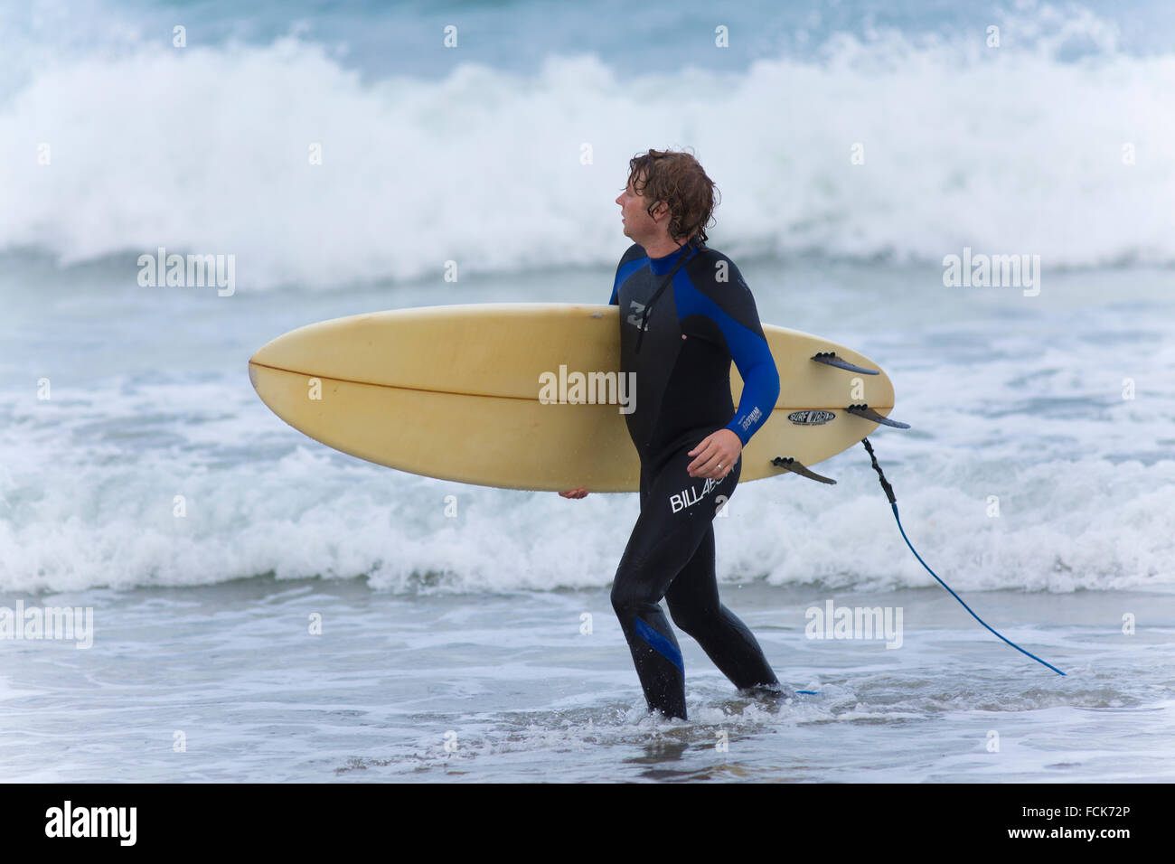 Surfer portano la sua tavola da surf attraverso le onde su Polzeath Beach Cornovaglia Foto Stock