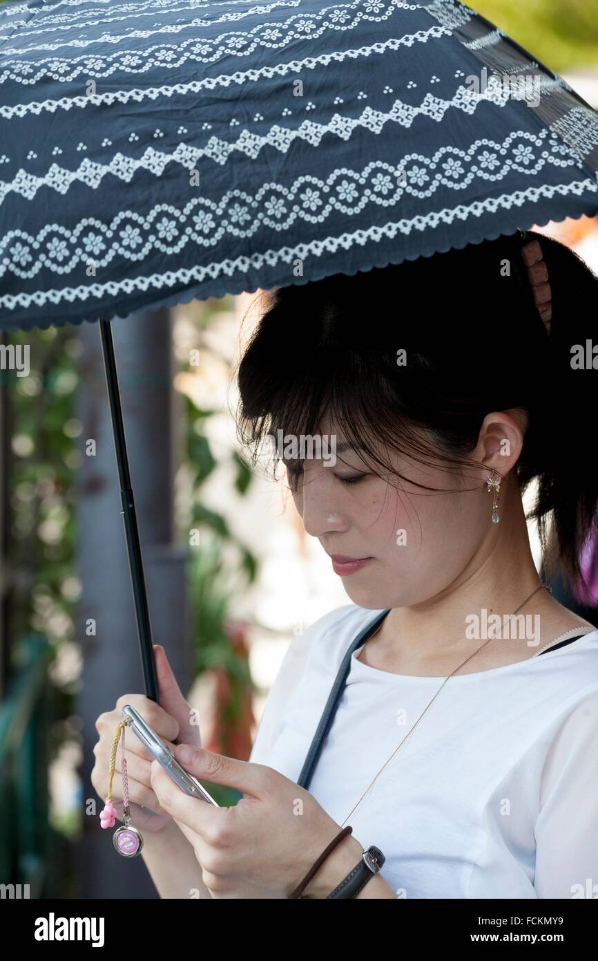 Bruna ragazza con ombrello e smartphone in Tokyo, Giappone Foto Stock