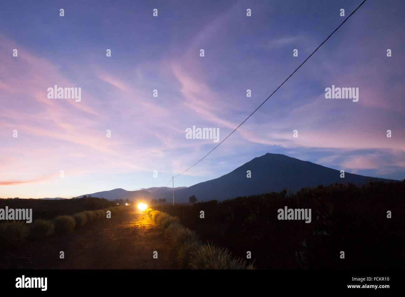 Dopo il tramonto, ammira il vulcano del Monte Kerinci e una strada con piantagione di tè a Kersik Tuo, Kayu Aro, Kerinci, Jambi, Indonesia. Foto Stock