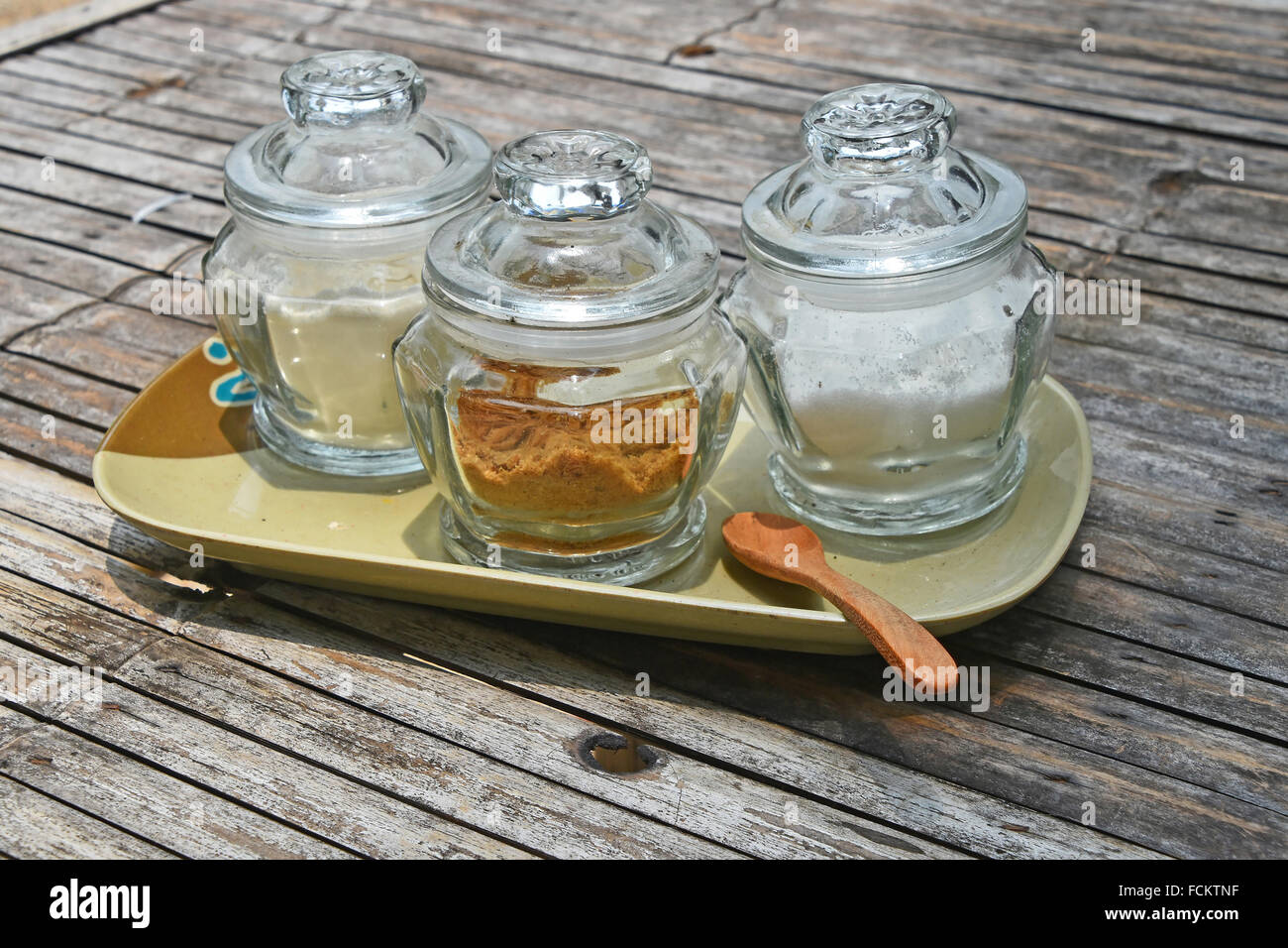 Tre vasi di vetro di zucchero differente, bianco e marrone di canna, sul piattino in ceramica con il cucchiaio di legno sul vecchio vintage tabella di bambù per c Foto Stock
