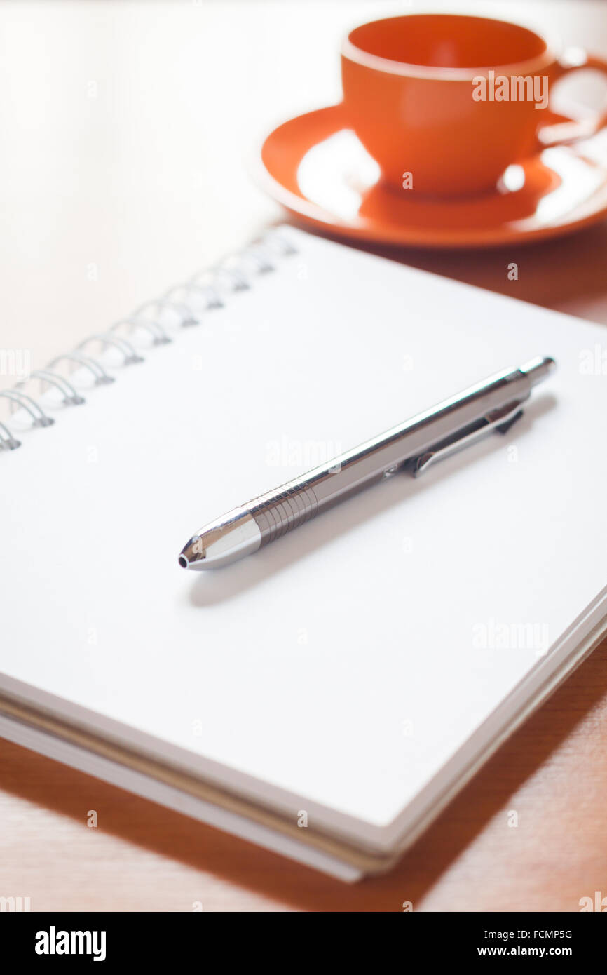 Penna sul fustellato aperto bianco per notebook con tazza di caffè sulla scrivania, stock photo Foto Stock