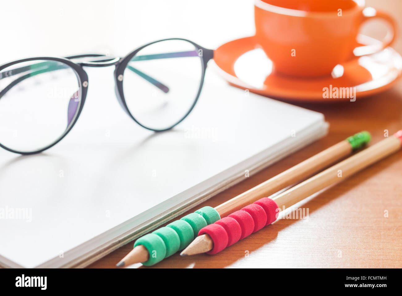 Matite e occhiali sul fustellato aperto bianco per notebook con tazza di caffè sulla scrivania, stock photo Foto Stock