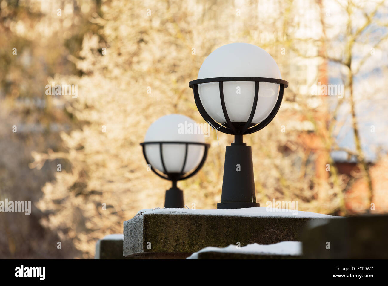 Lund, Svezia - 21 Gennaio 2016: due belle esterna sferica progettista luci adornano la parte superiore delle colonne in pietra. Frosty alberi fuori dalla f Foto Stock