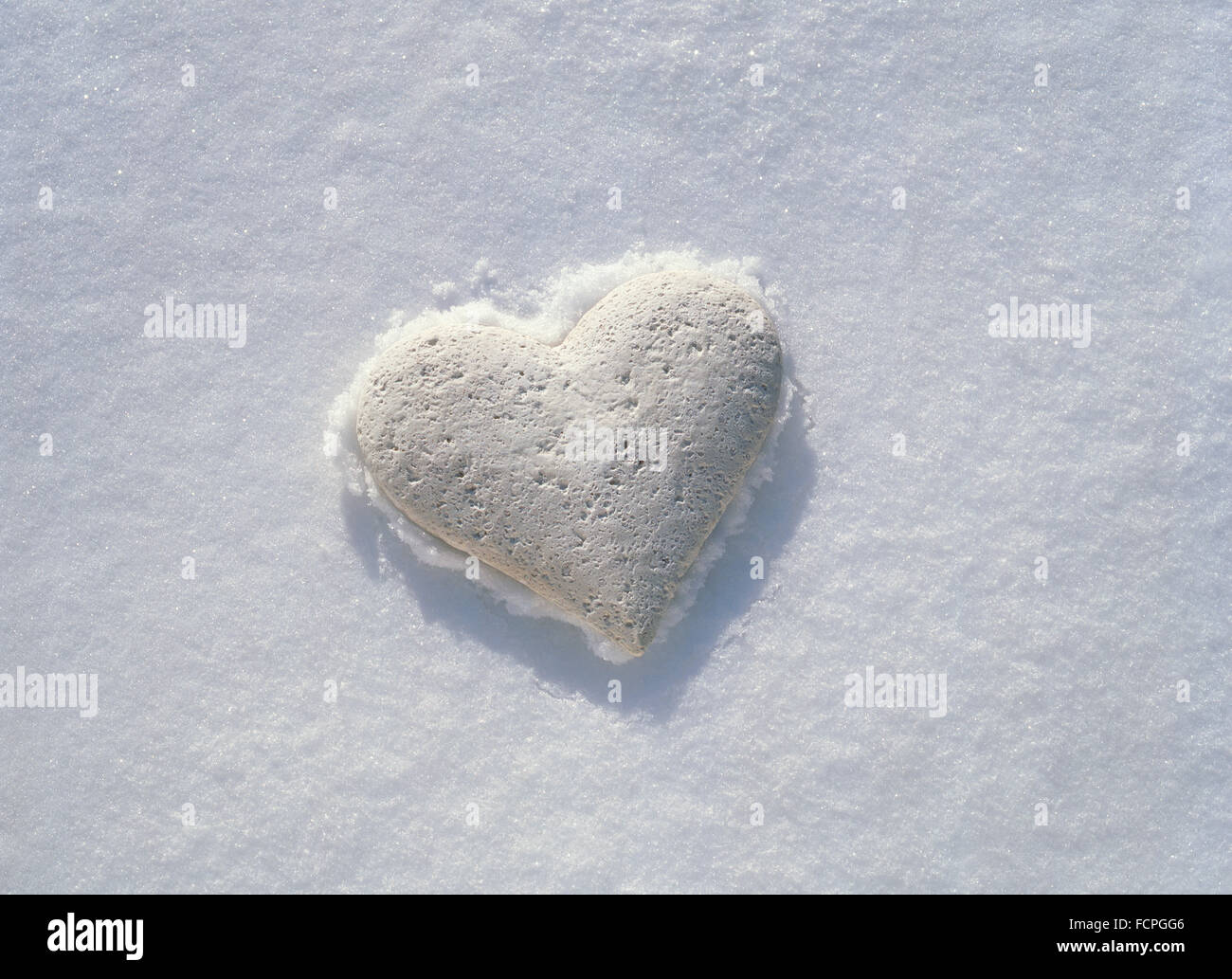 Bianco cuore di pietra in appoggio sulla crosta congelata di neve incontaminata. Foto Stock