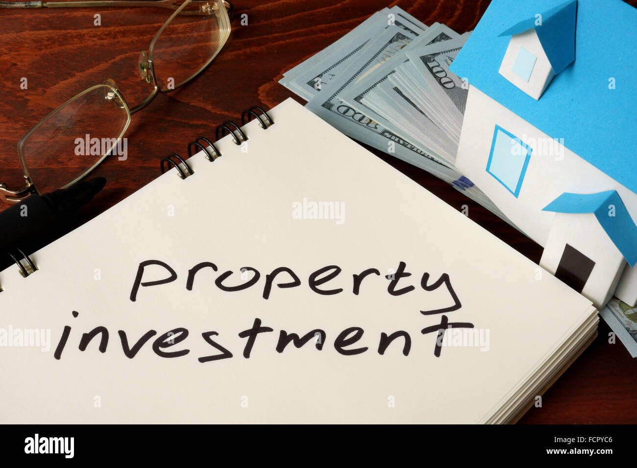 Gli investimenti immobiliari scritto su notebook con il modello di casa e di dollari. Foto Stock