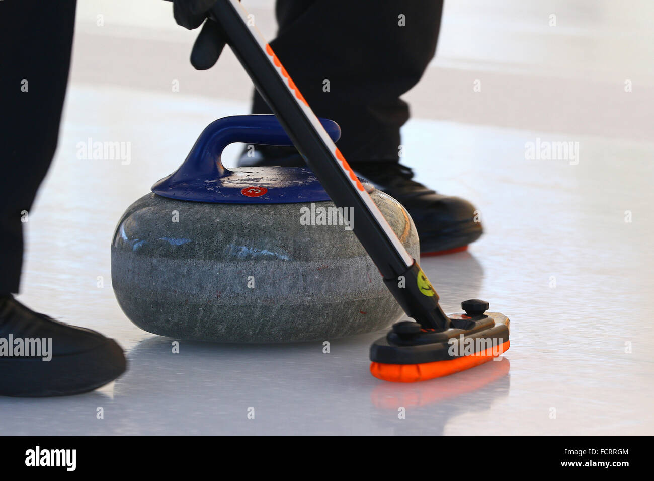 Pietra di Curling lo scorrimento verso il basso del ghiaccio con piede del calciatore in esecuzione nella parte anteriore di esso Foto Stock