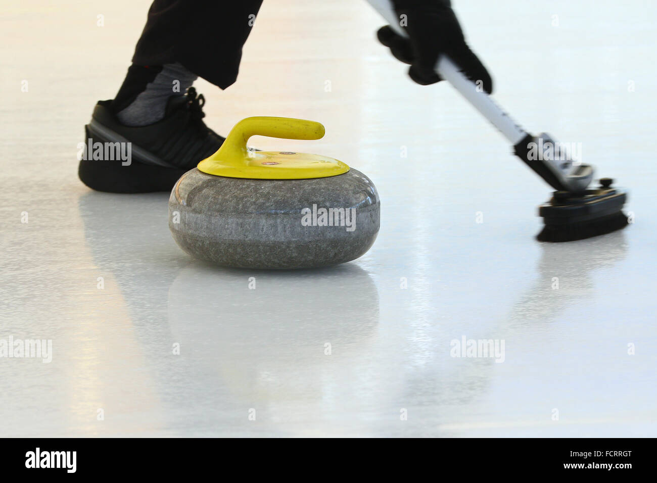 Pietra di Curling lo scorrimento verso il basso del ghiaccio con piede del calciatore in esecuzione nella parte anteriore di esso Foto Stock
