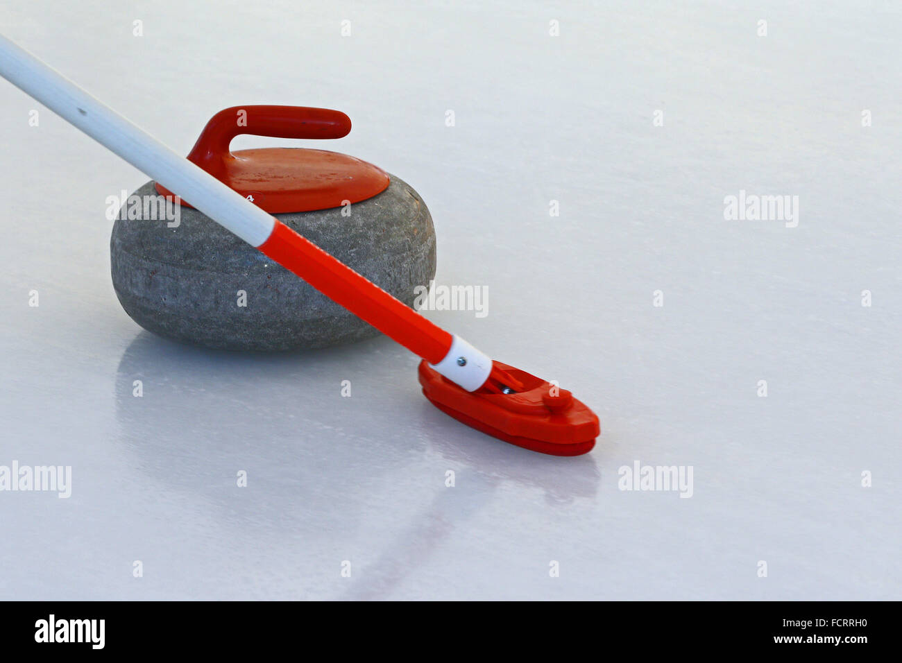 Pietra di Curling scivolare sul ghiaccio con il giocatore di scopa in parte anteriore di esso Foto Stock