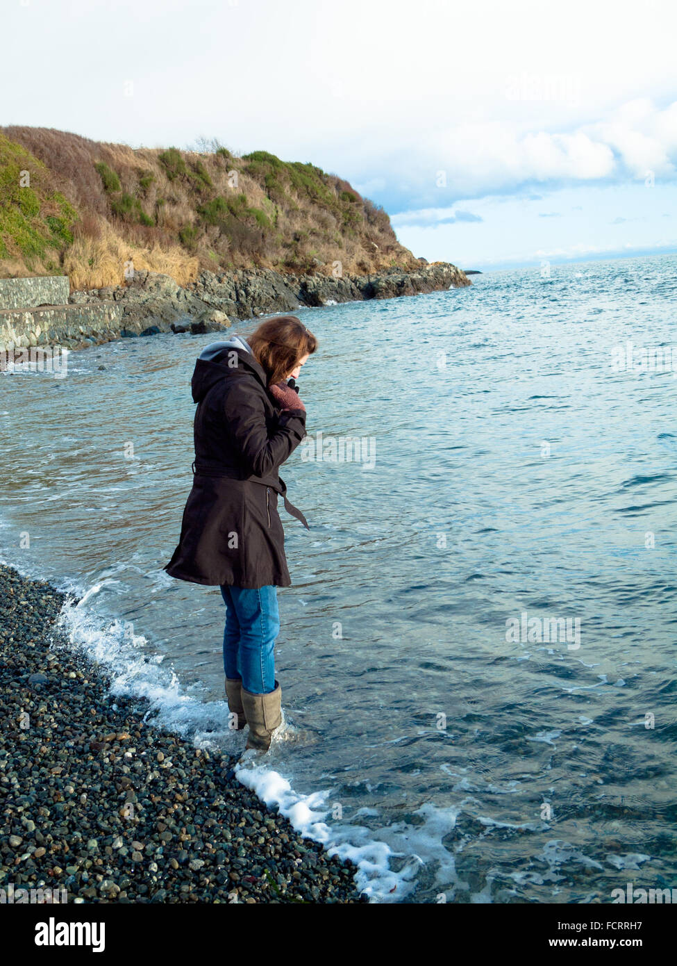 Una bella bruna ragazza, in stivali, wades nello stretto di Juan de Fuca off Victoria, British Columbia, Canada. Foto Stock