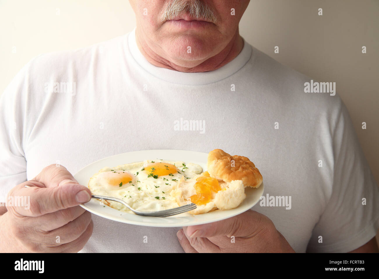 Un uomo con una colazione a base di uova fritte e un biscotto con marmellata di albicocche Foto Stock