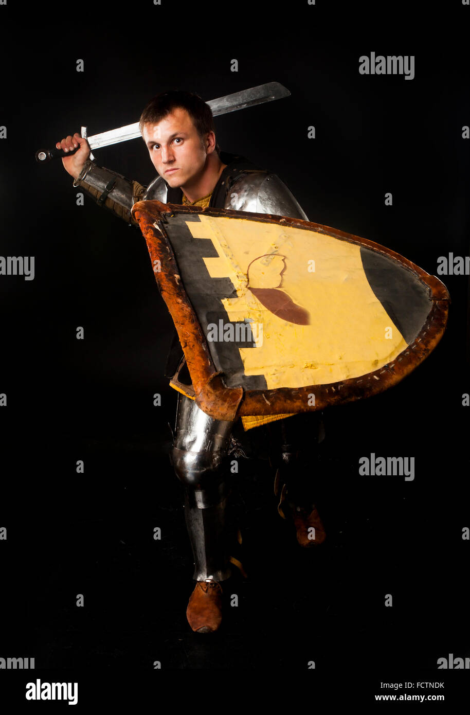 Studio shot del giovane uomo vestito da cavaliere medievale oscillando la sua spada per attacco cruciali Foto Stock
