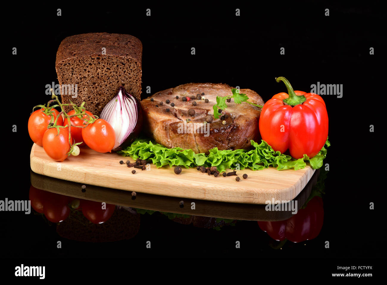 Gustosi piatti a base di carne medaglione con lattuga, cipolla, peperoncino, pomodoro e una pagnotta di pane su un tagliere di legno. Sfondo nero con Foto Stock