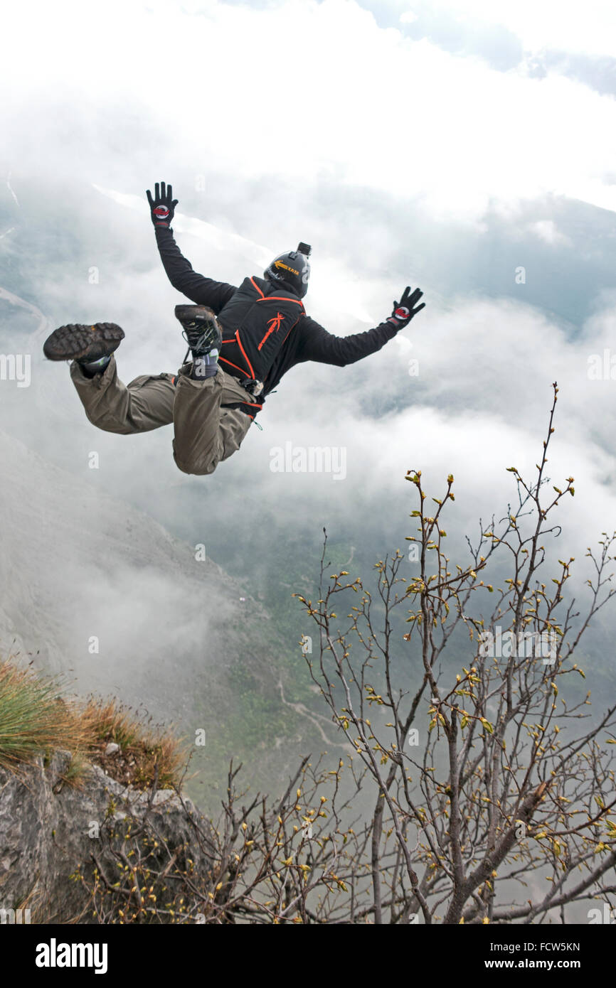 Questo uomo il rafforzamento di una rupe verso il basso, verso l'ignoto misty cloud. Speriamo che possa aprire il suo paracadute di base prima di terra!? Foto Stock