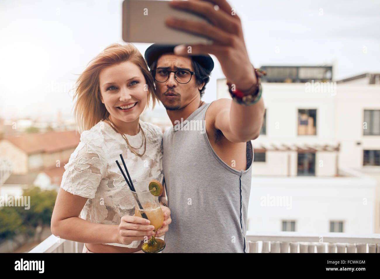 Coppia giovane tenendo autoritratto con smart phone durante una festa. Giovane uomo e donna prendendo selfie al partito sul tetto. Appendere o Foto Stock