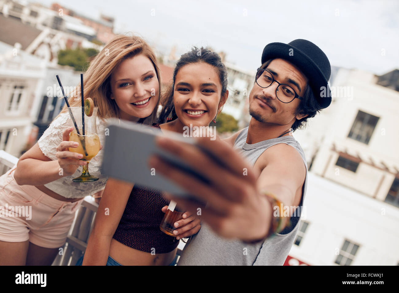 Multirazziale persone godendo in party con bevande e prendendo un autoritratto. Tre giovani amici prendendo selfie con smart phone Foto Stock