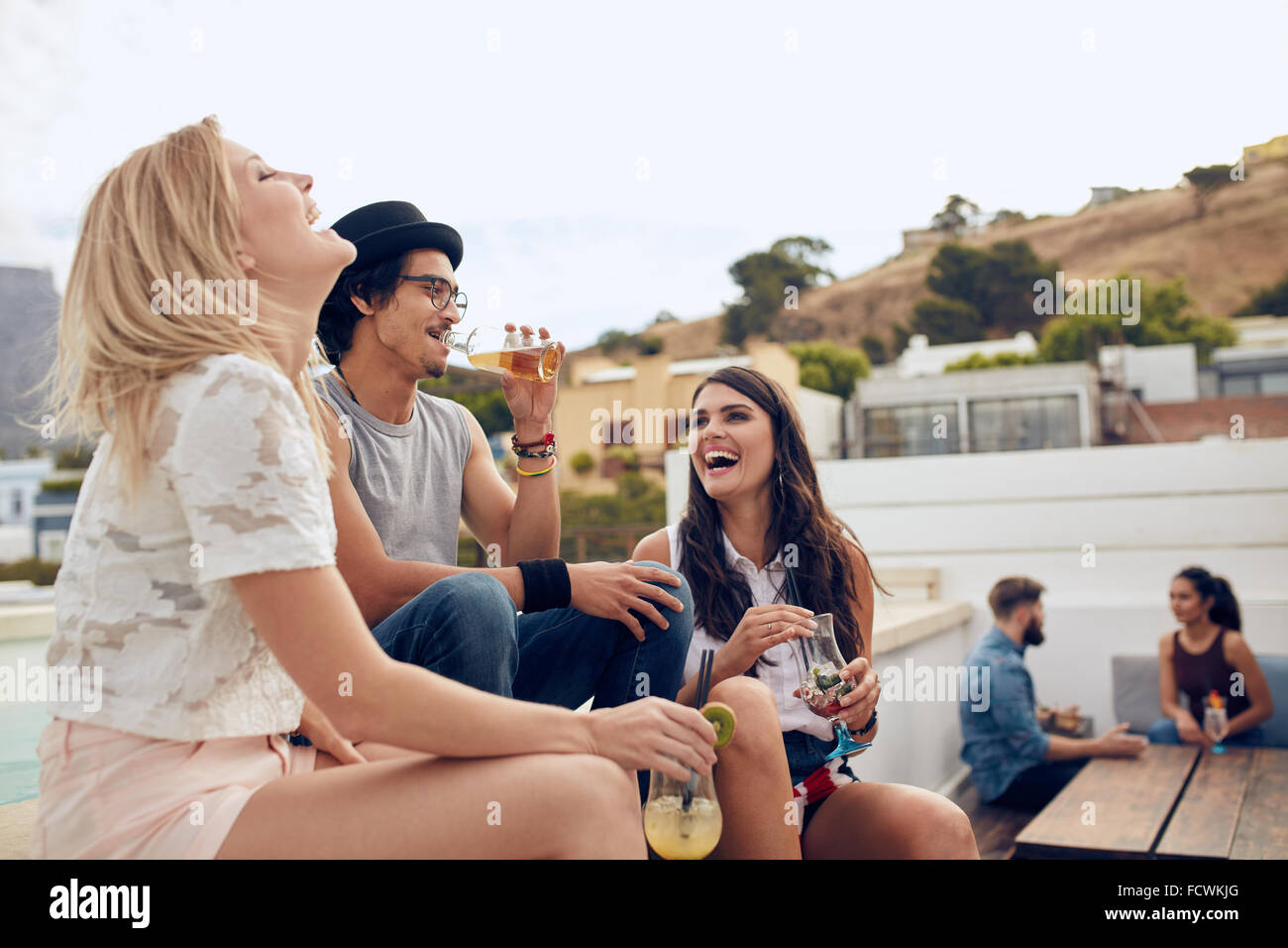Felice giovani con bevande e godendo mentre i loro amici seduti e di parlarsi in background. Giovani uomini Foto Stock
