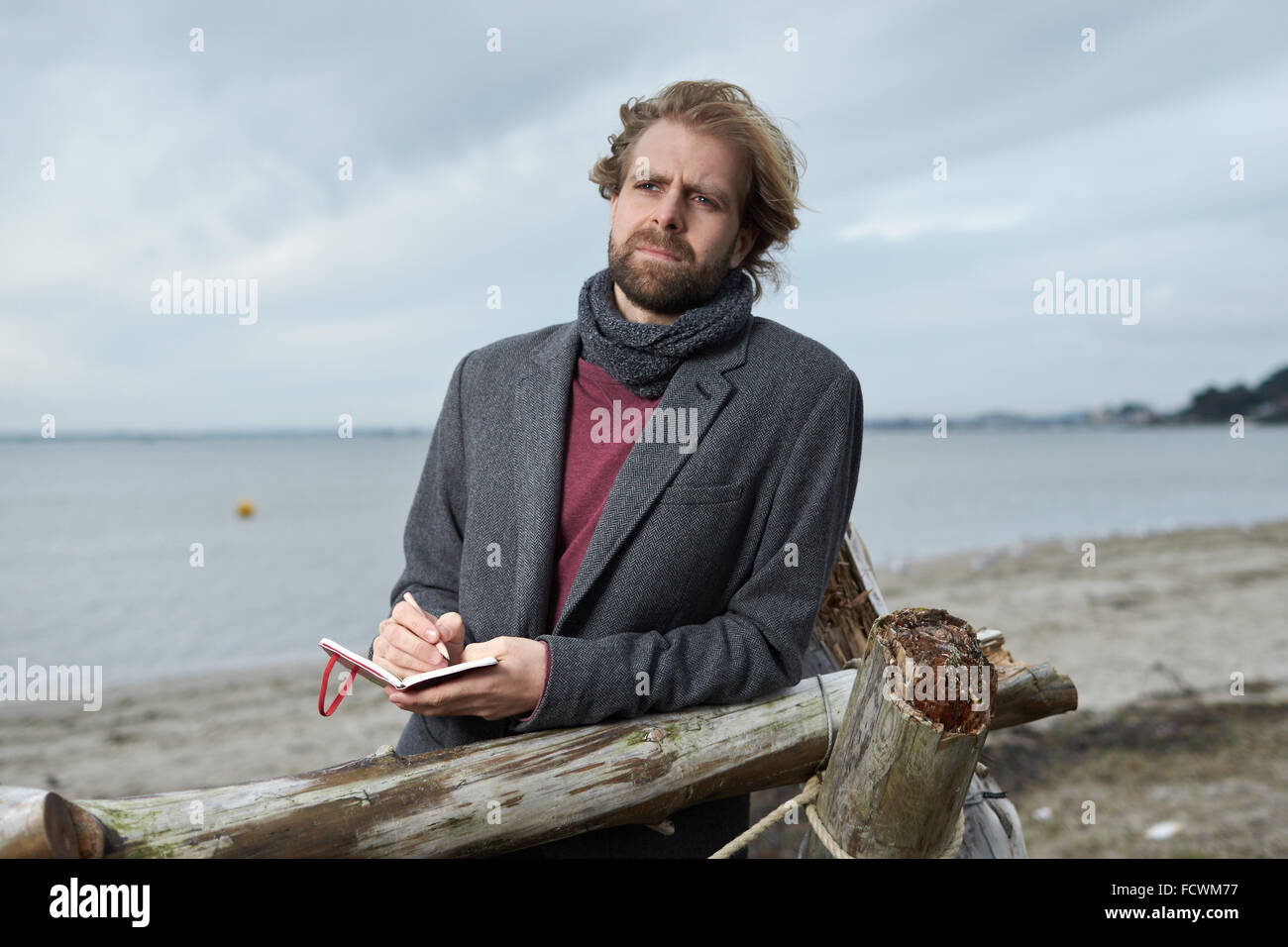 Un uomo che guarda pensieroso con un appunti da una spiaggia in inverno Foto Stock