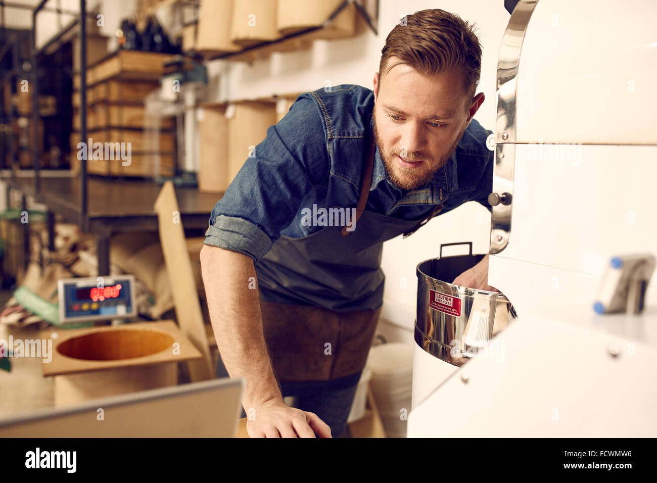 L'uomo controllando il suo computer portatile durante il funzionamento di un moderno di torrefazione del caffè Foto Stock