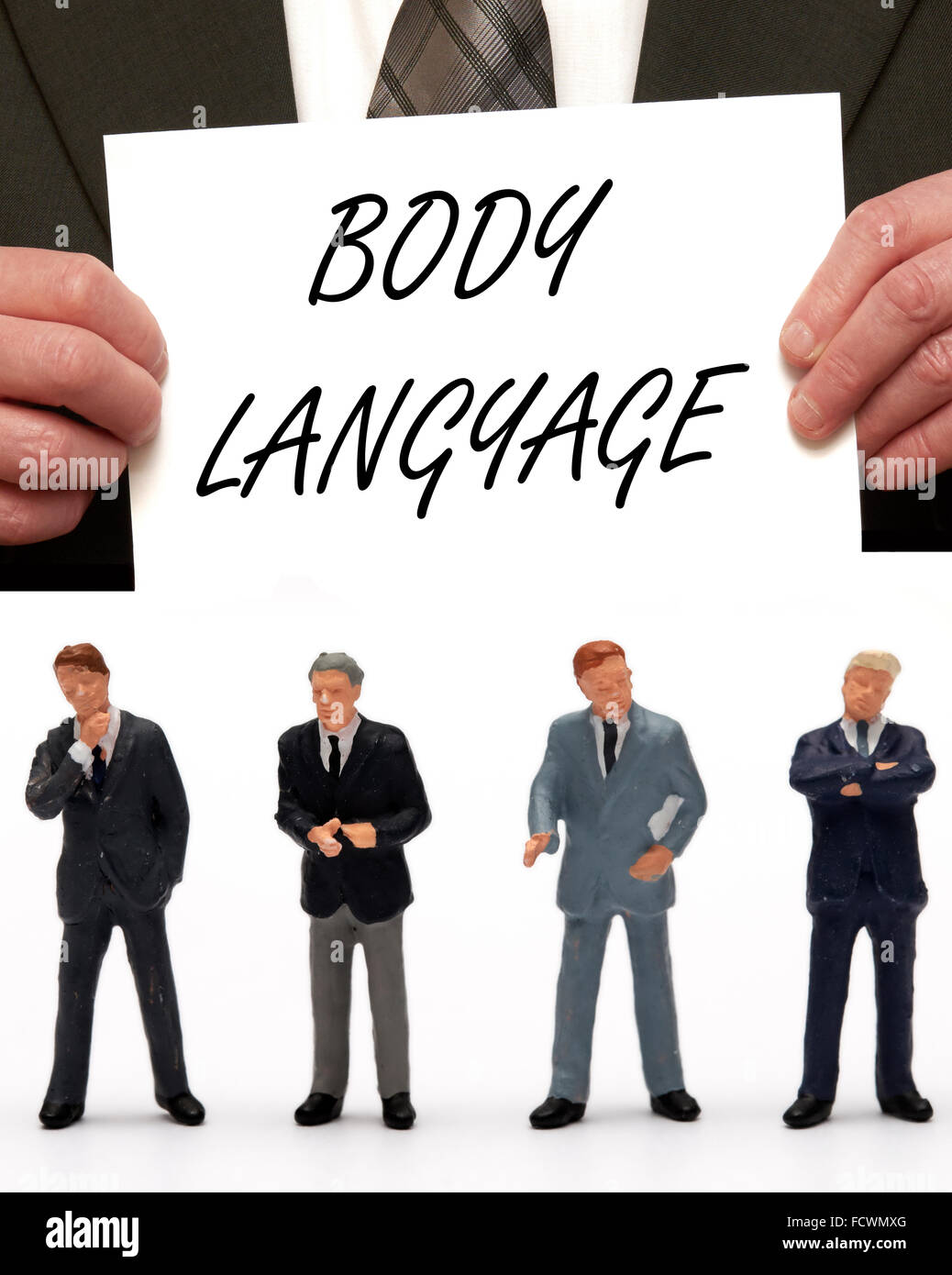 Statuetta in miniatura Business uomini vestiti in abiti sotto il messaggio " Il linguaggio del corpo' su una scheda che viene tenuto da un uomo in una tuta Foto Stock