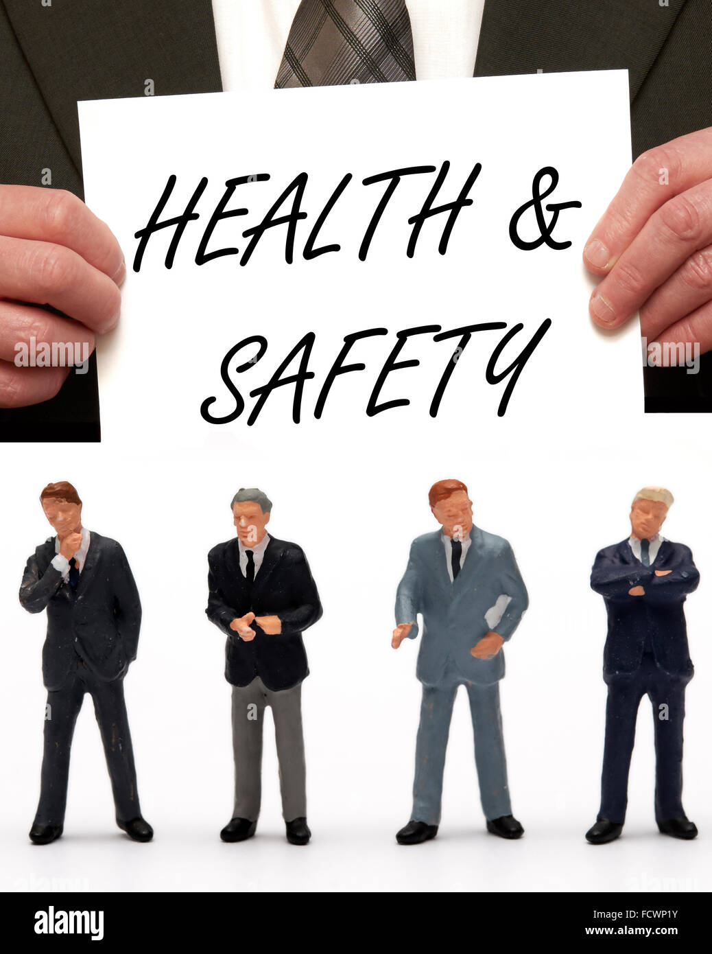 Statuetta in miniatura Business uomini vestiti in abiti con il messaggio di salute & sicurezza su una carta che viene tenuto da un uomo in una tuta Foto Stock