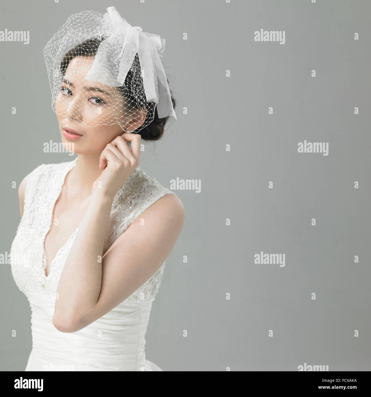 La donna in abito da sposa e un corto velo mesh guardando verso il basso con la mano sul suo viso Foto Stock