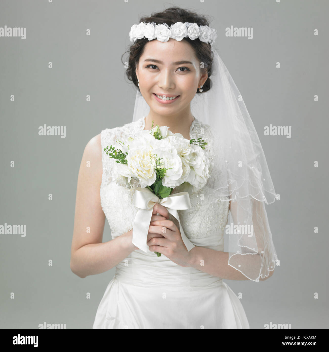 Sposa nella corona di fiori con il velo di pizzo tenendo un mazzo di fiori Foto Stock