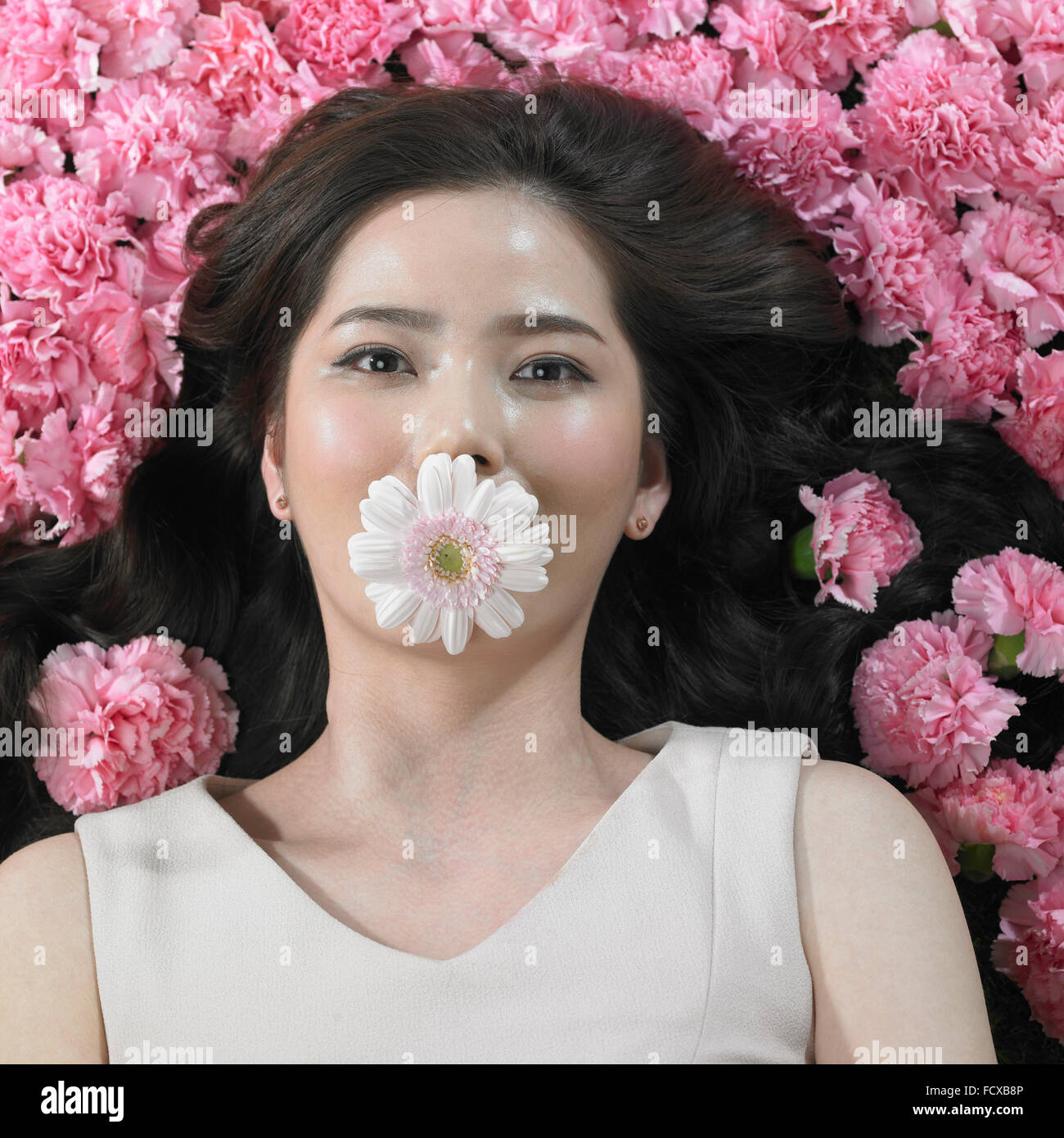 Elevato angolo di donna sdraiata su fiori di garofano con un fiore nella sua bocca con lo sguardo in avanti Foto Stock