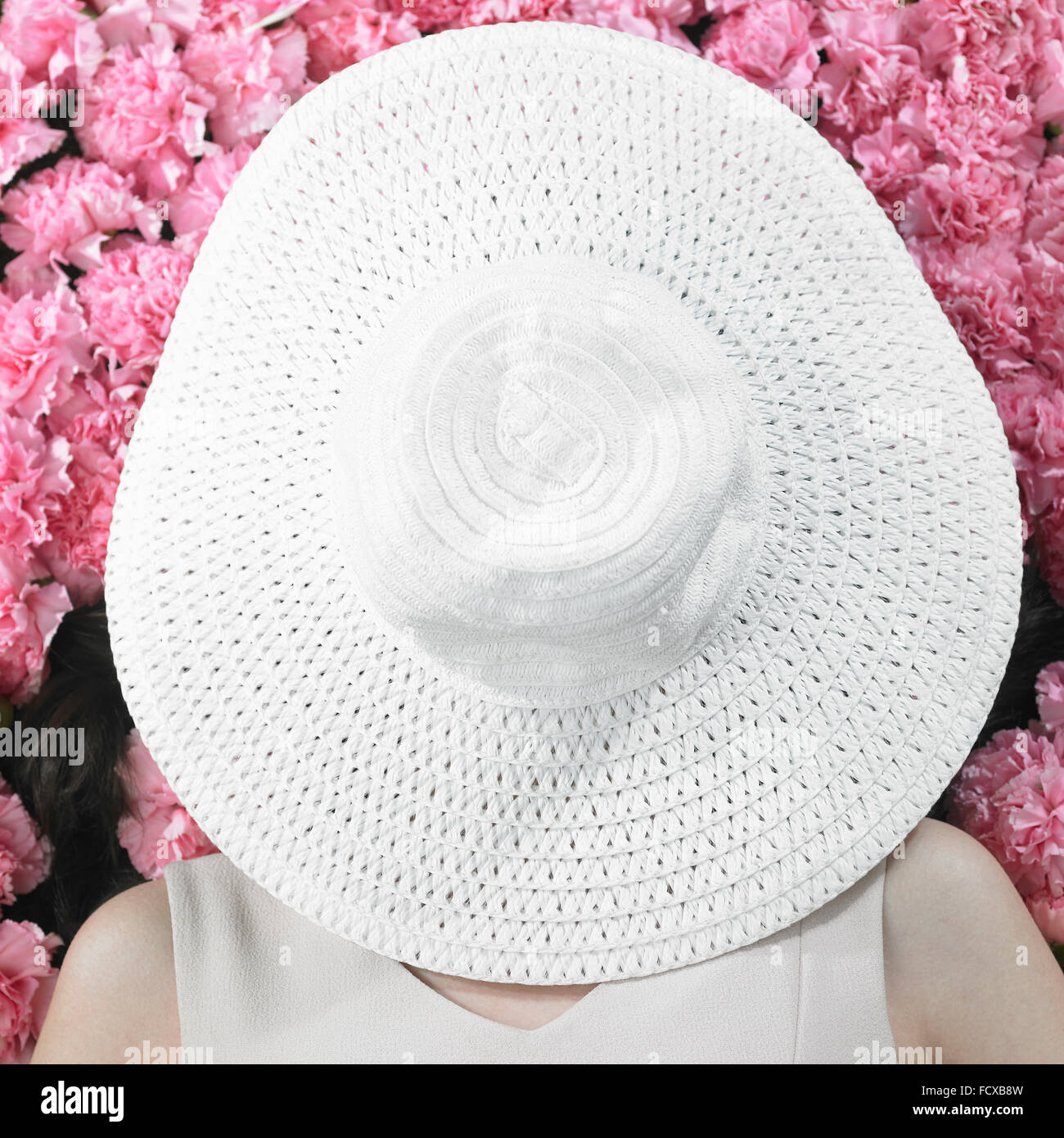Elevato angolo di donna sdraiata su fiori di garofano con un cappello che copre completamente il suo volto Foto Stock