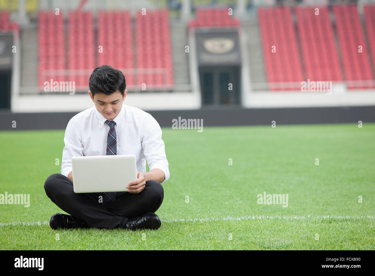 Spazio di copia con un uomo in business suit seduta sul campo di erba e di lavorare sul suo computer portatile Foto Stock