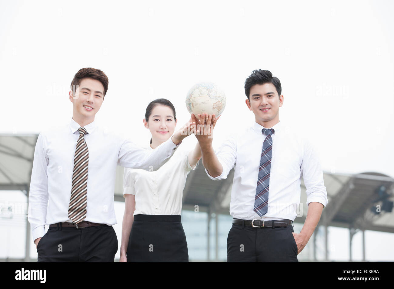 Due uomini e una donna tenendo un globo insieme con lo sfondo del campo sportivo Foto Stock