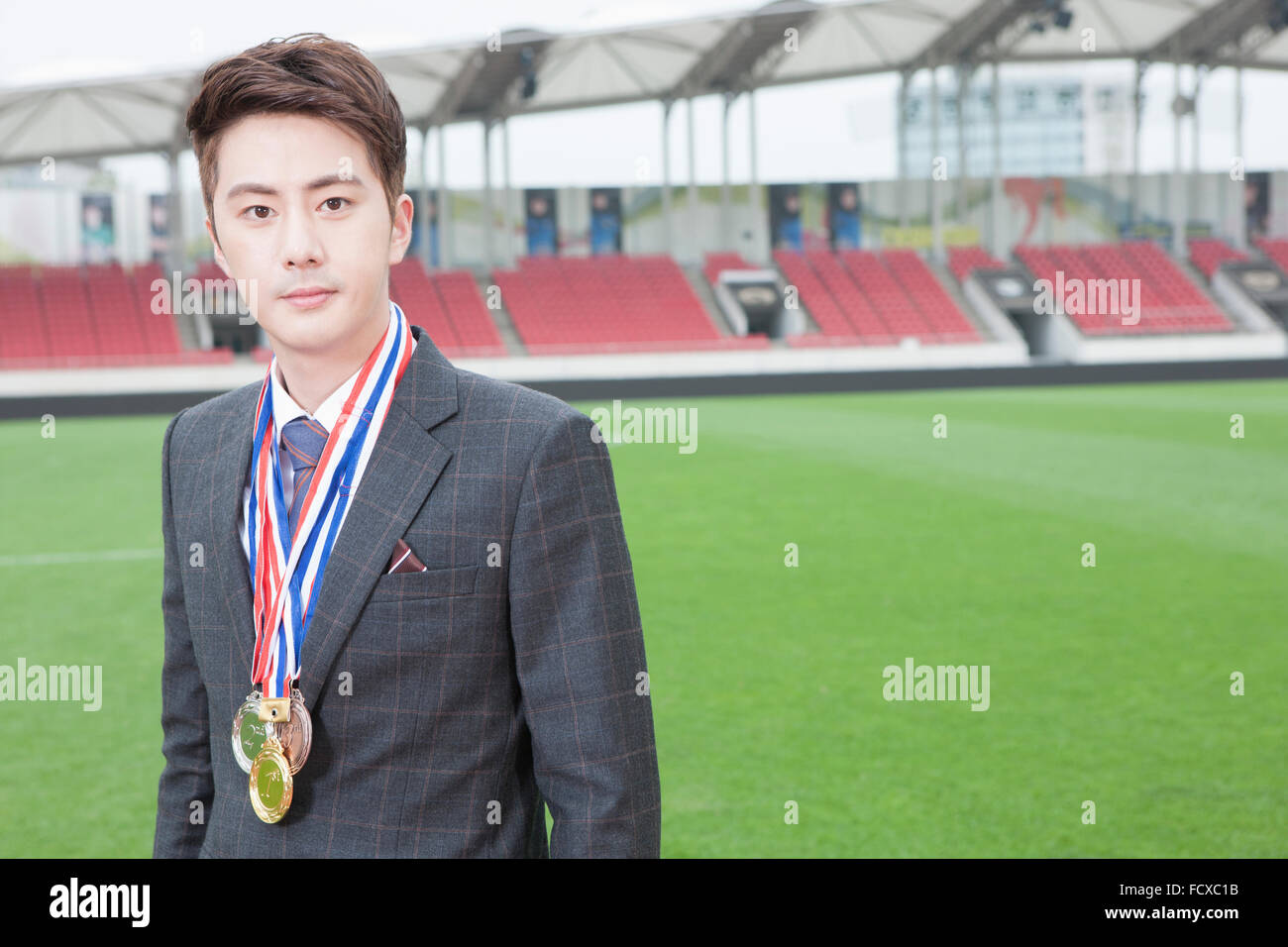 Spazio di copia con un uomo in business suit indossando la medaglia d'oro con lo sfondo del campo sportivo Foto Stock