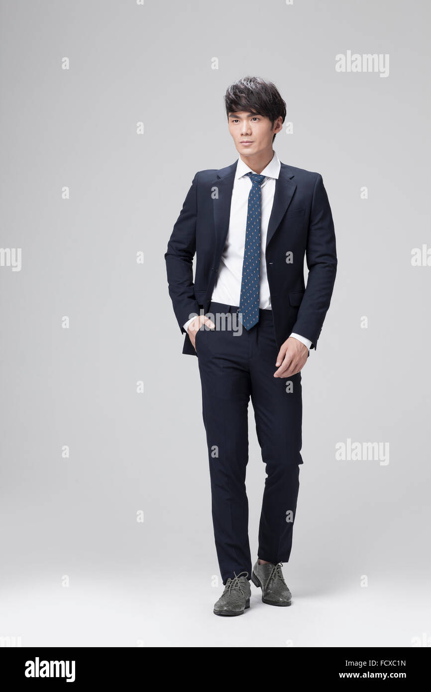 Uomo in abito nero in piedi e fissando con la mano in tasca Foto Stock