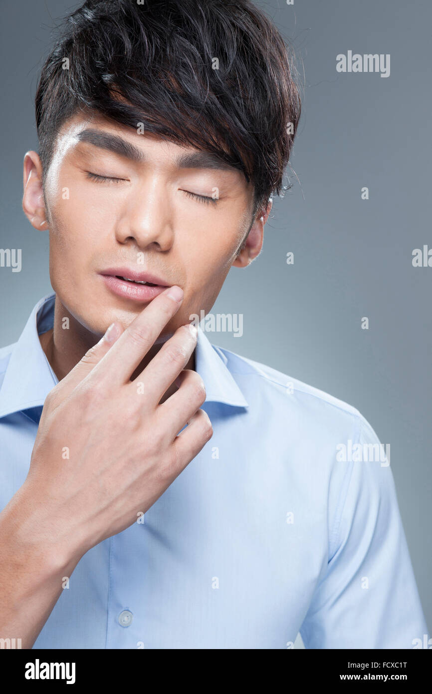 Uomo in camicia blu toccando il suo mento con gli occhi chiusi Foto Stock