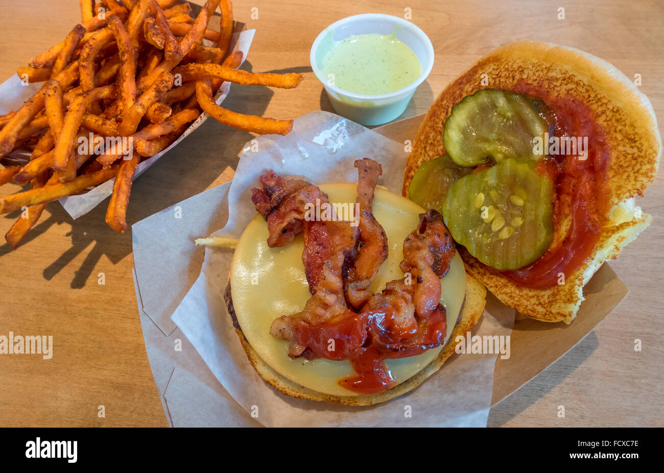 Un bacon cheeseburger con ketchup e sottaceti e la patata dolce patate fritte Foto Stock