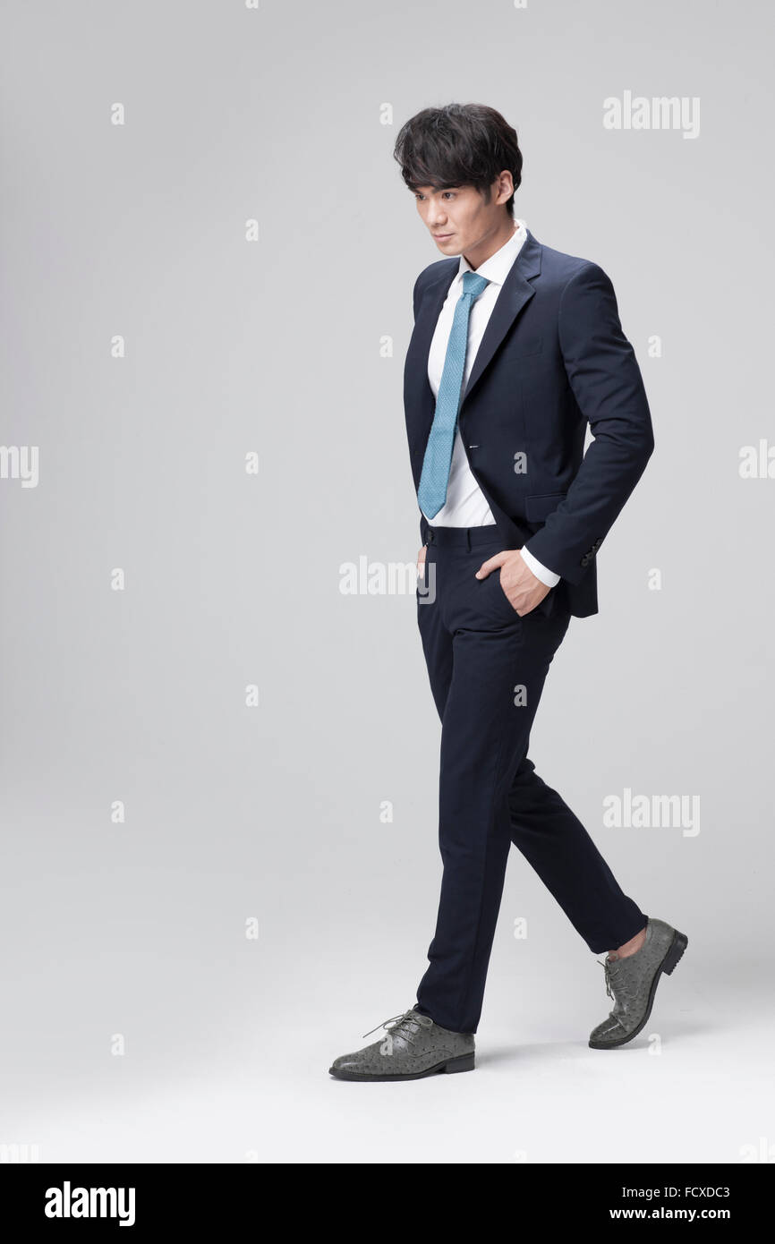 Uomo in abito nero e cravatta blu a piedi con le mani in tasca dei suoi pantaloni e guardando verso il basso Foto Stock