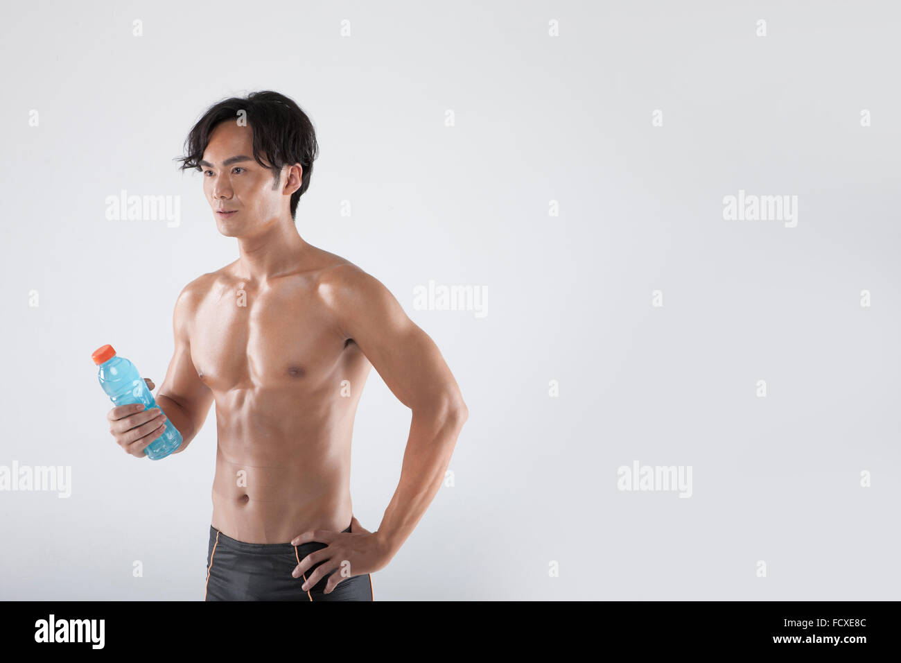 In topless di uomo in pantaloni fitness tenendo una bottiglia di bevanda con una mano sulla sua vita Foto Stock