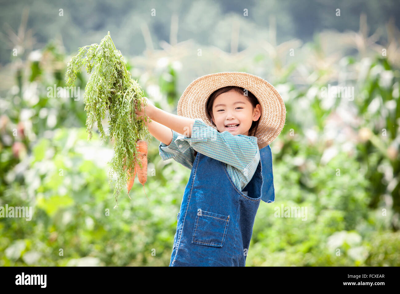 Ragazza in un cappello di paglia tenendo le carote fino e sorridente nel campo Foto Stock