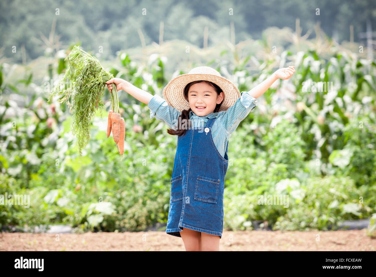 Ragazza in un cappello di paglia tenendo le carote fino e sorridente nel campo Foto Stock
