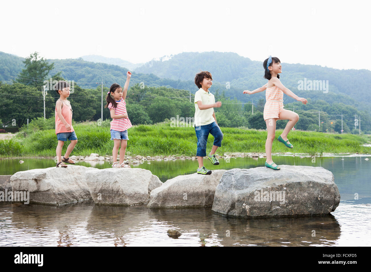 Quattro bambini passeggiate lungo le pietre miliari in una riga a stream Foto Stock