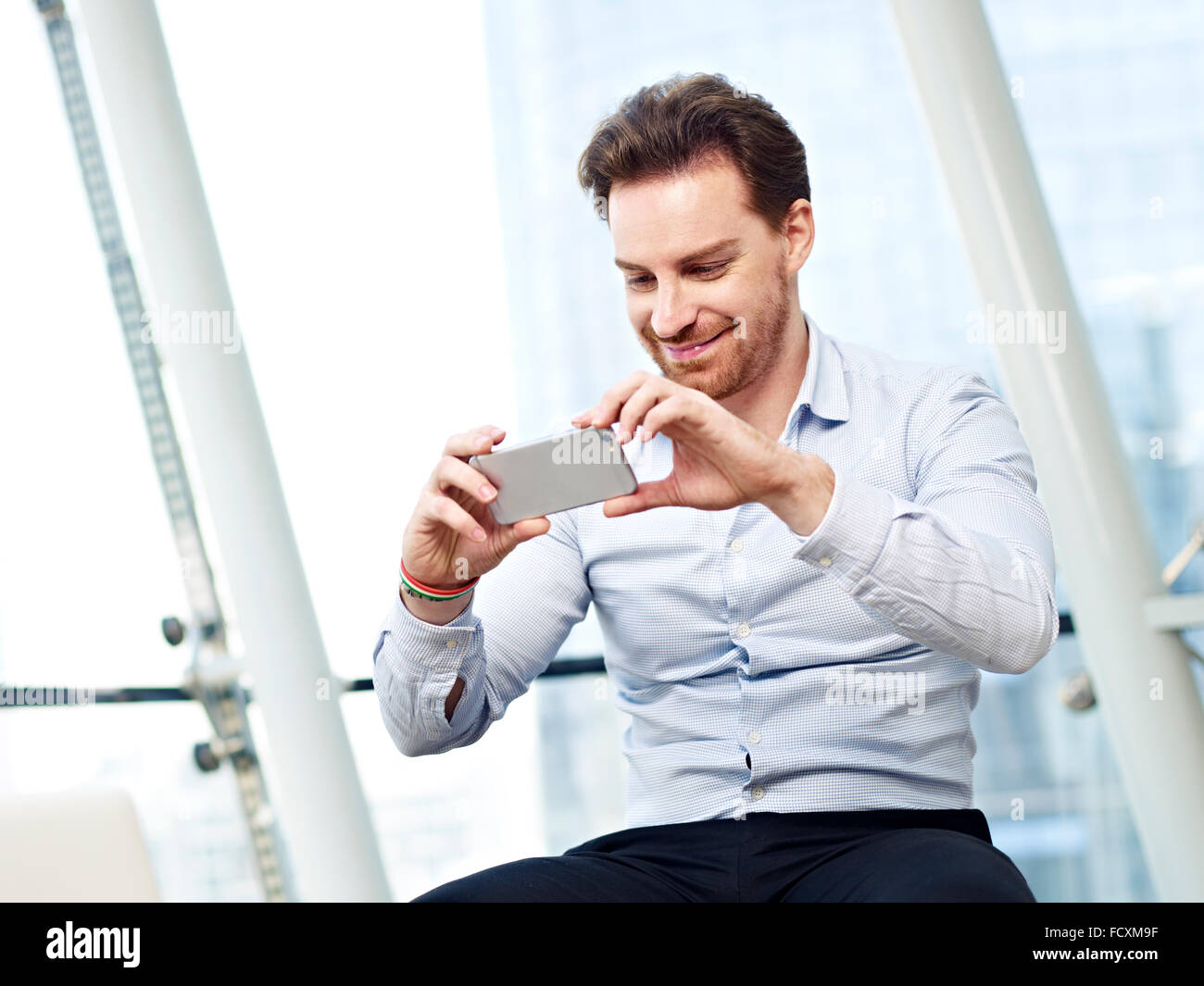 Giovani caucasici uomo business guardando una foto o guardare un video o scattare una foto con il cellulare e sorridente. Foto Stock