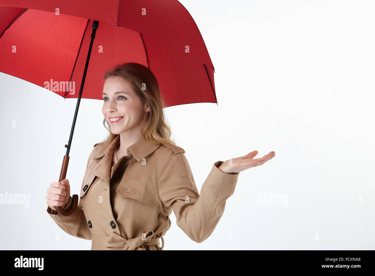 Veduta laterale Ritratto di giovane donna sorridente indossando ombrello rosso e trench tenendo la mano Foto Stock