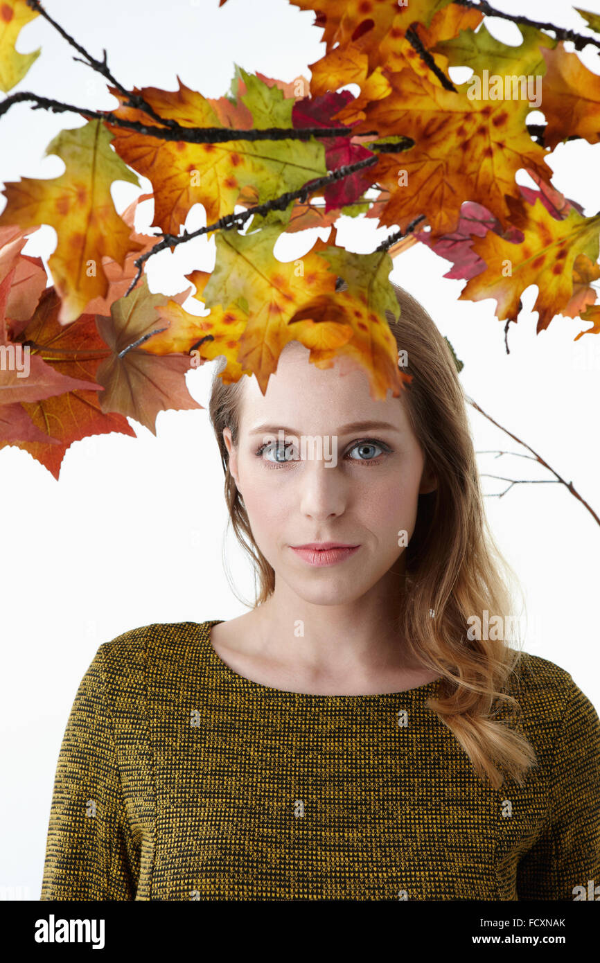 Ritratto di giovane donna con capelli lunghi con lo sguardo fisso anteriore sotto le foglie di autunno Foto Stock