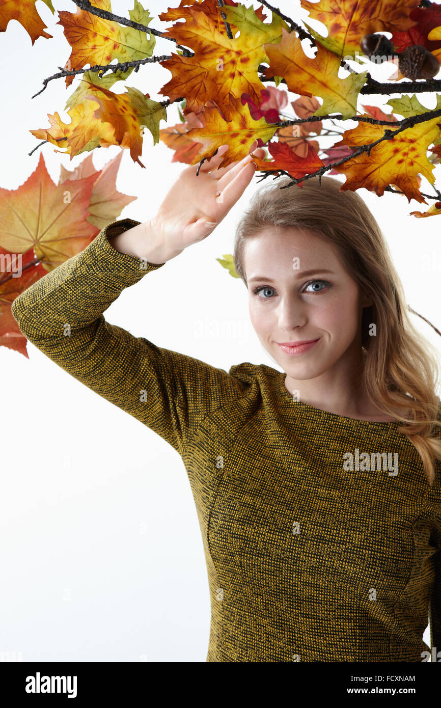 Ritratto di giovane donna sorridente con i capelli lunghi toccando le foglie di autunno stairng sulla parte anteriore Foto Stock