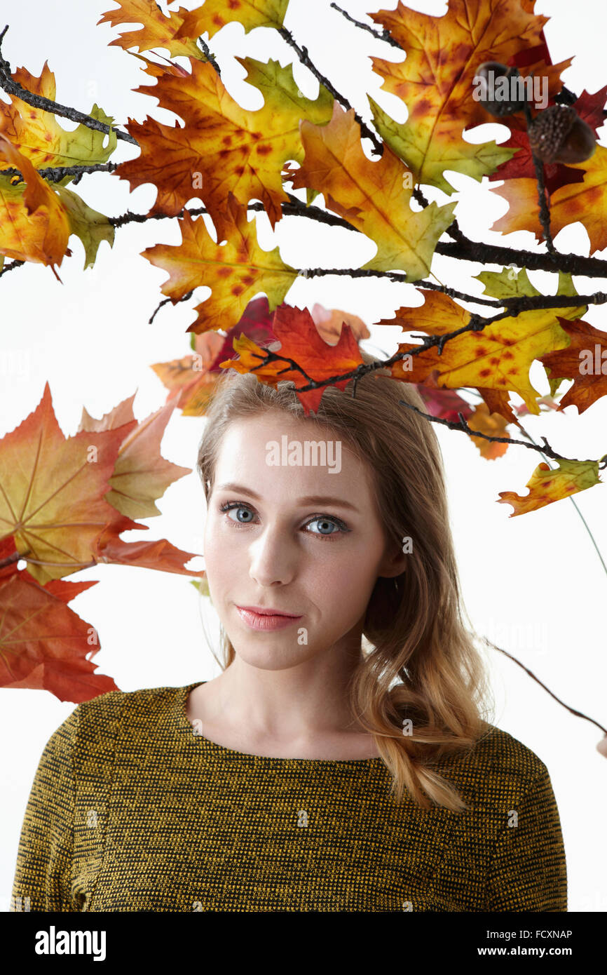 Ritratto di giovane donna con capelli lunghi con lo sguardo fisso anteriore sotto le foglie di autunno Foto Stock